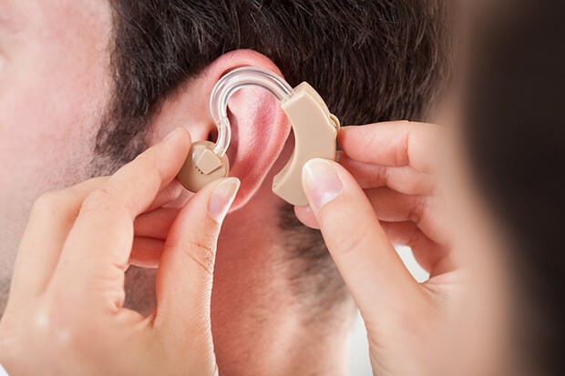 Close-up Of Hand Helping Young Man To Wear Hearing Aid